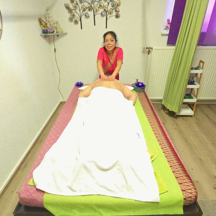 Thaimassage auf der Bodenmatte: Die Masseurin arbeitet am Rücken, der Gast liegt zugedeckt