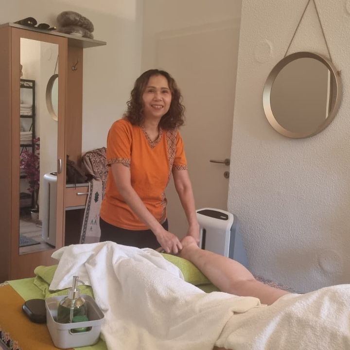 Beinmassage im Behandlungsraum: Die Masseurin arbeitet am Bein eines zugedeckten Gastes