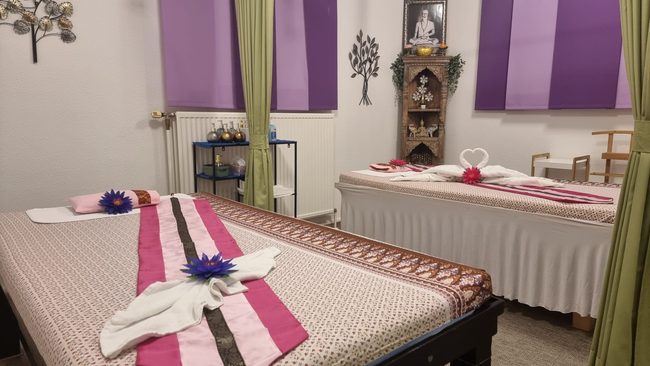 Behandlungsraum mit zwei Massageliegen, violetten Wandpaneelen und einem kleinen Buddha-Altar