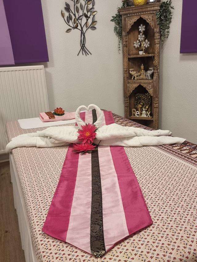 Behandlungsraum mit Massageliege, zu Schwänen gefalteten Handtüchern und hölzernem Altar mit Buddha-Figur